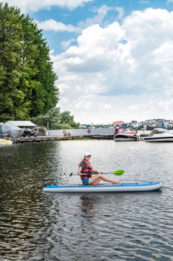 an experienced athlete in a vest rides on the water on a board sap on the lake in sunny beautiful weather. The concept of a healthy lifestyle