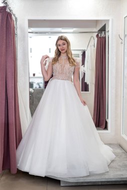 Happy woman trying on elegant wedding dress in a wedding salon, dreaming bride