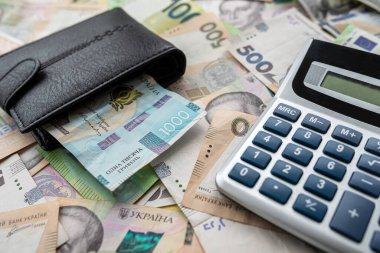 many euro and hryvnia banknotes lie on the table next to a wallet with money and a calculator on the table. Currency concept