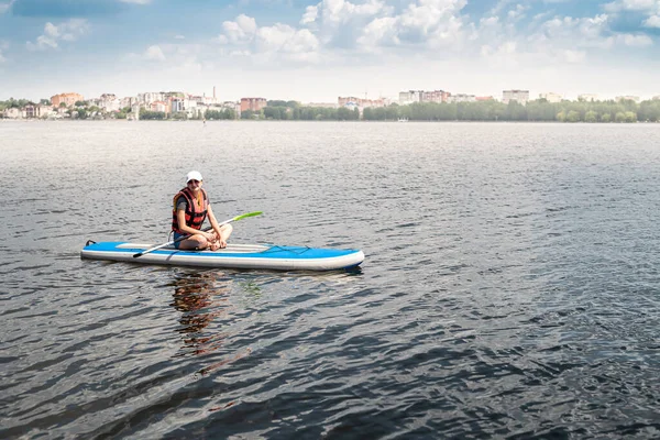 an experienced athlete in a vest rides on the water on a board sap on the lake in sunny beautiful weather. The concept of a healthy lifestyle