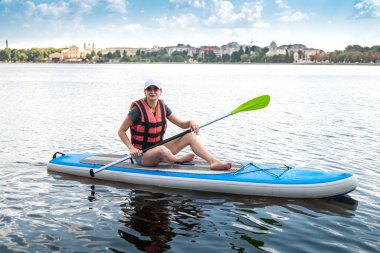 beautiful pumped-up athlete poses on the water on a board and catches the sun's rays on her body. The concept of extreme sports