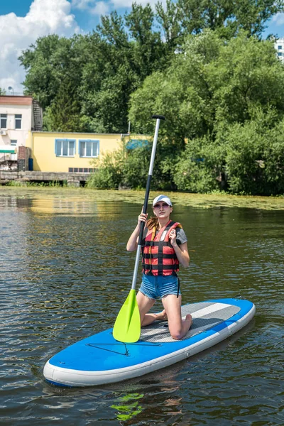 Young woman sitting on paddle board wear life vest and learn how swim, summer active lifestyle