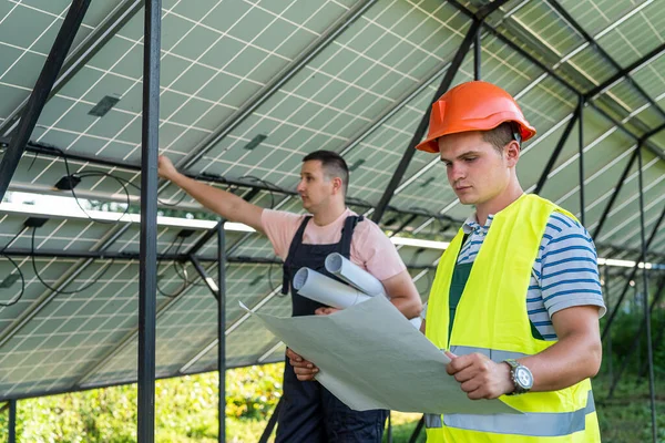 two young courageous workers in uniform stand under solar panels. Green electricity concept