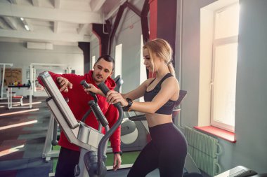 Spor merkezinde kişisel antrenörüyle koşu bandında koşan formda bir bayan müşteri. Sportif yaşam tarzı