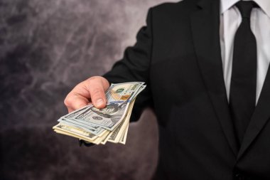 a man with a strong physique in a shirt and jacket holds his own earned dollar bills. The concept of a good big profit in dollars