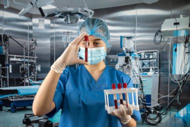 Üniformalı maske takan çekici ve deneyimli bir doktor. Eldiven takıyor. Hastanedeki ameliyathanede kan sondalarını inceliyor.
