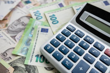 many euro and Ukrainian hryvnia banknotes are scattered around the table with a calculator to determine the exchange rate. Currency exchange concept