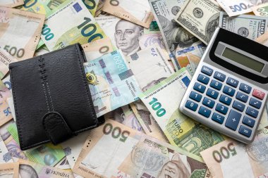 many euro and hryvnia banknotes lie on the table next to a wallet with money and a calculator on the table. Currency concept