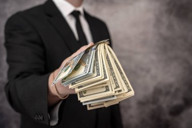 İşadamı, pahalı takım elbisesinin cebine dolar banknot parası koyuyor. İş ve kâr kavramı