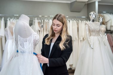 A pretty sales consultant measures a wedding dress for a client and shows impeccable quality. Bridal store