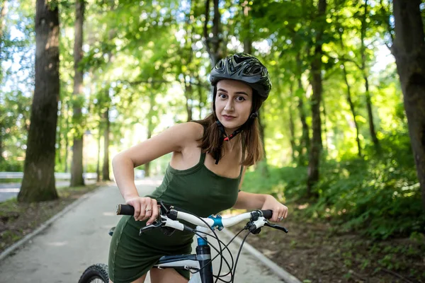 Fitness girl wear green dress rides a modern mountain bike in forest at hot summer day. Activity freedom and relaxation lifestyle