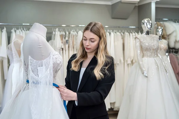 A pretty sales consultant measures a wedding dress for a client and shows impeccable quality. Bridal store