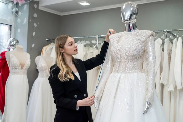 Şık siyah takım elbiseli çekici kadın satıcı gelinliği butikle ölçer.