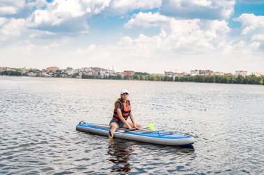 beautiful pumped-up athlete poses on the water on a board and catches the sun's rays on her body. The concept of extreme sports