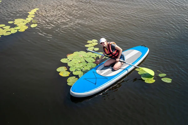 pretty sporty girl learn swim in life vest sitting with paddle on a board in city lake, summer lifestyle