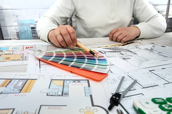 male architect designer in the office selects a palette of colors for drawings of the house on the project. Man's hands on the table with color palettes. Choice of colors from the palette