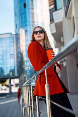 a young woman drinks coffee on the city streets of a metropolis in autumn or early spring. Business woman concept