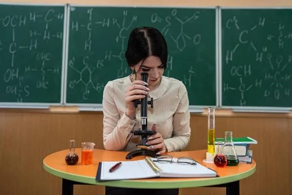 young teacher with microscope, book and test tubes in a classroom. chemistry lesson