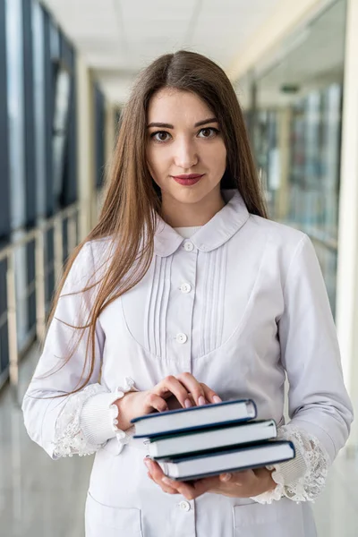 Smiling female doctor holding a book or magazine and walking down the med corridor to examine patients. Portrait of a female doctor. Medicine saves lives. A beautiful nurse