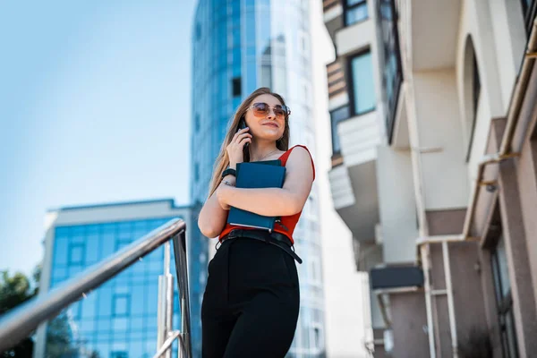 Portrait of a confident woman in elegant casual clothes and using a smartphone on a city street. Manager in a big city. Communication with people on the Internet.
