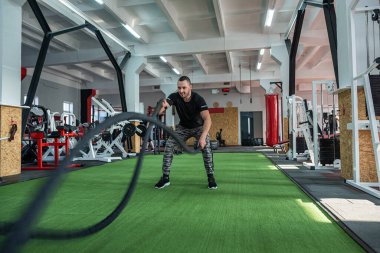 Harika fiziksel formda kas baskısı olan seksi erkek antrenör genç müşteriler için antrenman yapıyor. Seksi bir eğitmenin gözetiminde eğitim kavramı.