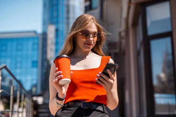 Portrait of a confident woman in elegant casual clothes and using a smartphone on a city street. Manager in a big city. Communication with people on the Internet.