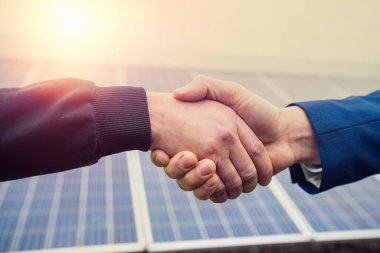 Tulum ve kask takmış iki işçi panel planını tamamladıktan sonra el sıkışıyor. Yeşil elektrik kavramı
