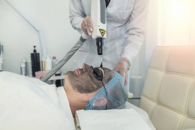 Güzellik uzmanının, spa salonundaki rahatlatıcı bir kadının yüzüne kilden bir maske taktığını hayal et. Gülümseyen genç bayan müşterinin en iyi görüntüsü. Kozmetoloji cilt prosedürleri