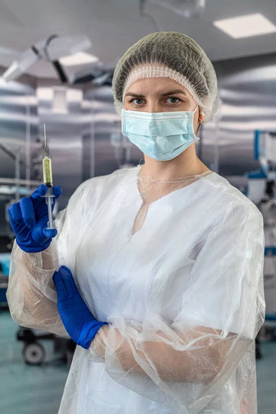 Portrait of a female doctor in a face mask wearing gloves prepares a syringe with medicine in the operating room. Healthcare concept. Preparation for surgery. patient\'s health