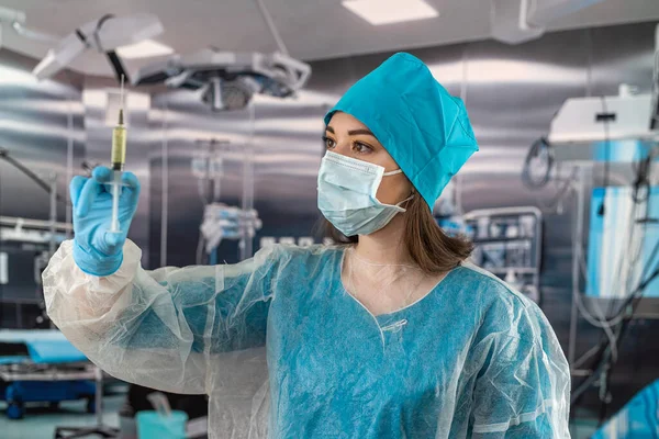 Portrait of a female doctor in a face mask wearing gloves prepares a syringe with medicine in the operating room. Healthcare concept. Preparation for surgery. patient\'s health