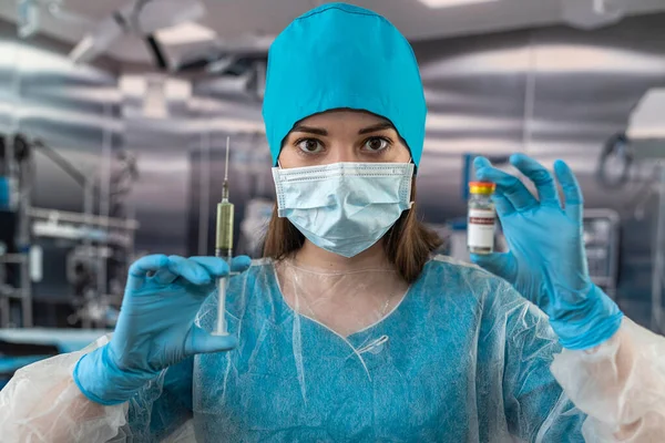 Portrait of a female doctor in a face mask wearing gloves prepares a syringe with medicine in the operating room. Healthcare concept. Preparation for surgery. patient's health