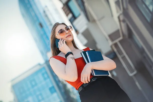 A beautiful business woman with a mobile phone is walking in the buildings in the city center. Woman and smartphone concept.