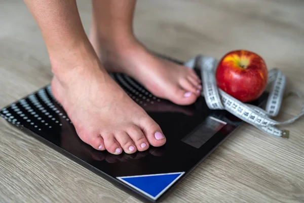 Cropped image of woman standing on scales against measuring tape and apple. We wrap the legs with a tape measure. body weight measurements. female feet