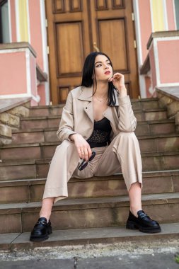 Modaya uygun genç bir kadın şehrin eski klasik evine karşı beyaz deri ceket giyiyor..