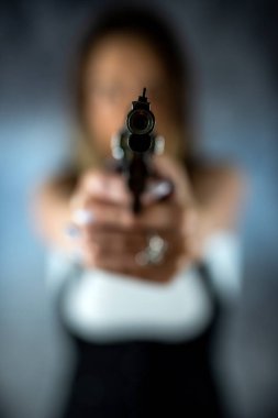 Genç, güzel, seksi esmer kadın elinde silahla arka planda poz veriyor. Silahlı bir kadın. Silah ellerinde.