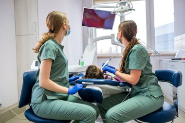 Diş hekimi ve asistanı çocuğun dişlerini bir kamerayla inceler ve resmi ekranda gösterirler. Bir çocuğu dişçide muayene etme konsepti