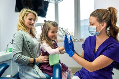 little girl's mother and dentist soothe little girl before dental treatment. The concept of approach to children in dentistry