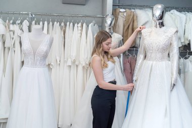 Kadın terzi, vitrindeki yeni gelinliği ölçmek için mezura kullanır.