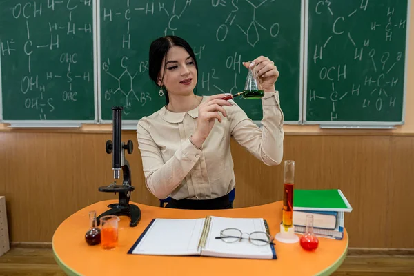 young teacher with microscope, book and test tubes in a classroom. chemistry lesson
