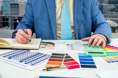 Adam oda tasarımı için renkleri seçiyor. Ofisteki yaratıcı masasına renkli kumaş ve dizüstü bilgisayarlı modern daireler çiziyor. Tasmaları tasarımcının elleri alıyor. Tasarımcı bir erkek.