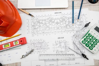 Bina planları kask ve çizim aletleriyle çiziliyor. Çizimler üzerindeki inşaat araçları