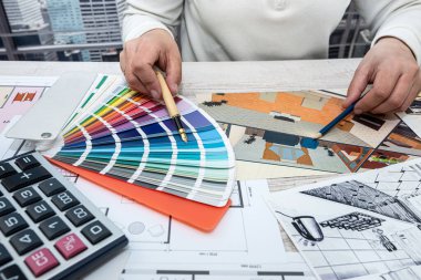 male architect designer in the office selects a palette of colors for drawings of the house on the project. Man's hands on the table with color palettes. Choice of colors from the palette
