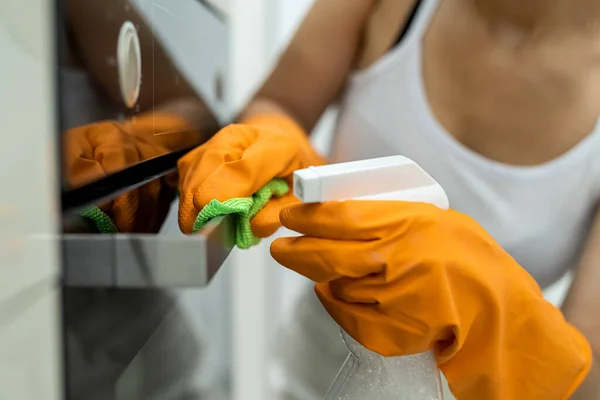 Female hands in gloves with bottle of detergent cleaning kitchen oven
