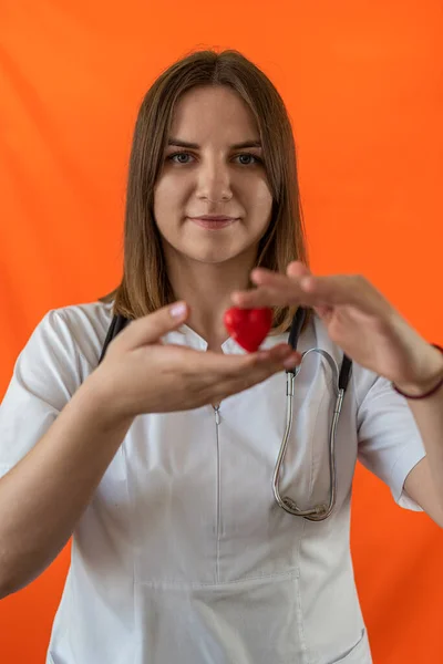 Young female doctor in hospital clothes mask and gloves holding a small red heart as a symbol in the hospital. Operational. Nurse. Heart symbol