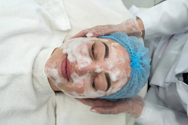 Cosmetologo Applica Una Maschera Nera Sul Viso Una Bella Donna — Foto Stock