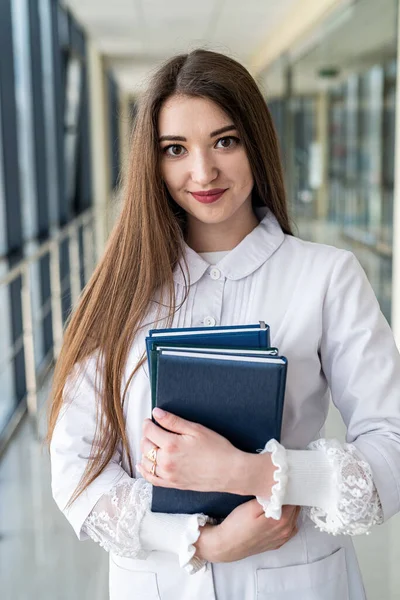 身着制服的年轻女医生的垂直肖像 听诊器拿着医学书籍 站在一边 望着别处 医学的概念 — 图库照片