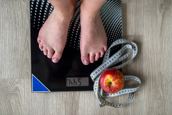 Cropped image of woman standing on scales against measuring tape and apple. We wrap the legs with a tape measure. body weight measurements. female feet