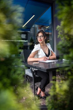 An attractive business lady is using her laptop while sitting outdoors on the terrace of a typical cafe. Businesswoman concept. Work on a laptop