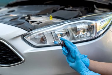 Çalışkan elleri olan tamirci arabanın farının yanında bir halojen ampul tutuyor. Bir tamirci tarafından araba tamiri. Bir halojen lamba değiştirmek