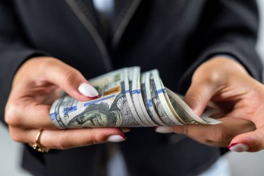 Kadın eli ceketinde banknotlar yığını görünüyor ve arka planda izole bir şekilde kutlanıyor. Eldeki para. İş kadını. Bayan patron.